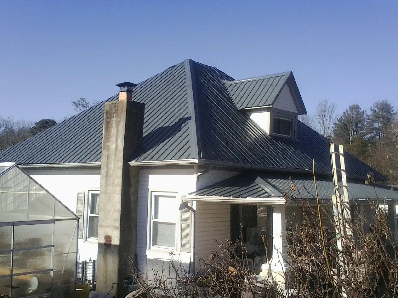 Dark blue standing seam metal roof on a white farmhouse with dormer — Slate & Tile Roof Repair by Roofing Brothers in Chilhowee