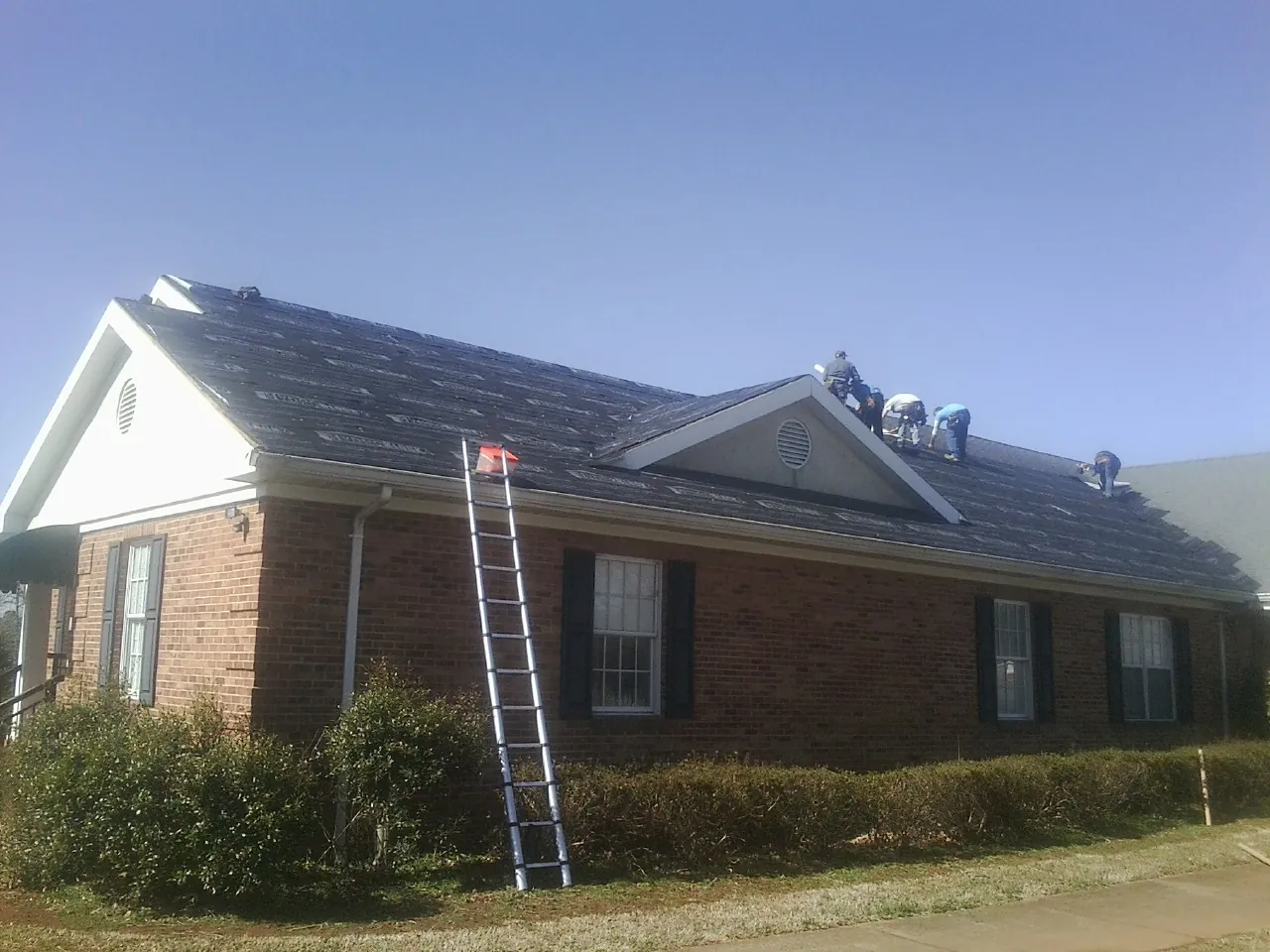 Crew tearing shingles off a brick ranch roof with a ladder set — Emergency Roof Repair work by our crew in Chilhowee