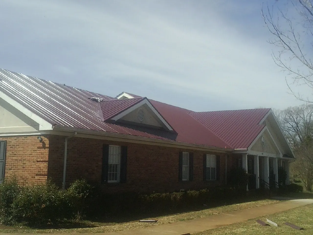 Red metal roof with gabled entries on a long brick building, from a Hail Damage Roof Repair job in Chilhowee