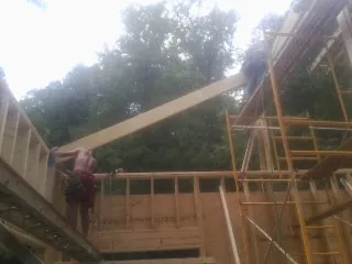 Carpenter raising a rafter beam on a new second story frame in Chilhowee