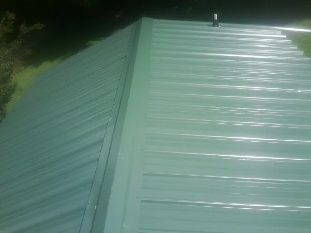 New green metal panels meeting at the ridge of a roof — Flat Roof Repair work by our crew in Chilhowee