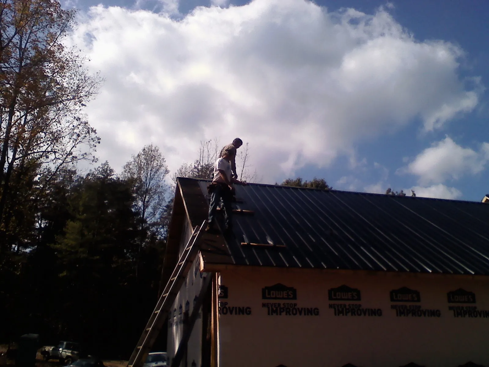 Roofer fastening dark metal panels high against a cloudy sky, from a Roof Inspection job in Chilhowee