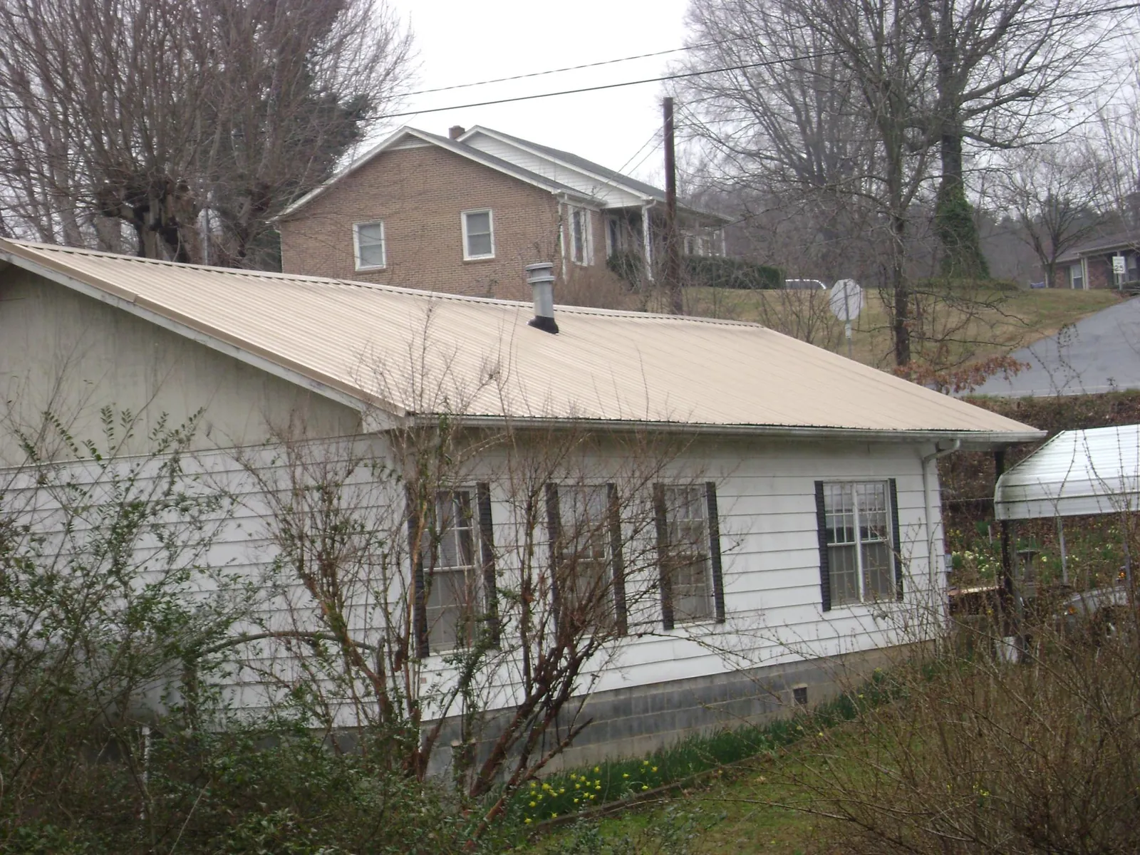 Tan metal roof on a white sided house set into a hillside — Commercial Roofing by Roofing Brothers in Chilhowee
