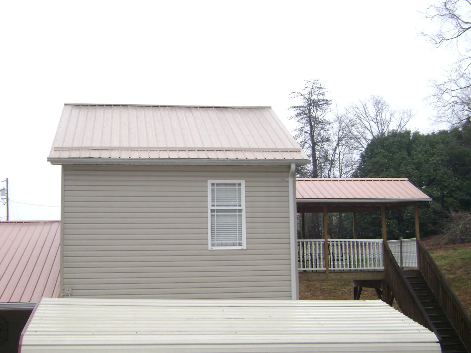 Tan metal roofs on a two story addition and attached porch, from a Roof Replacement job in Chilhowee